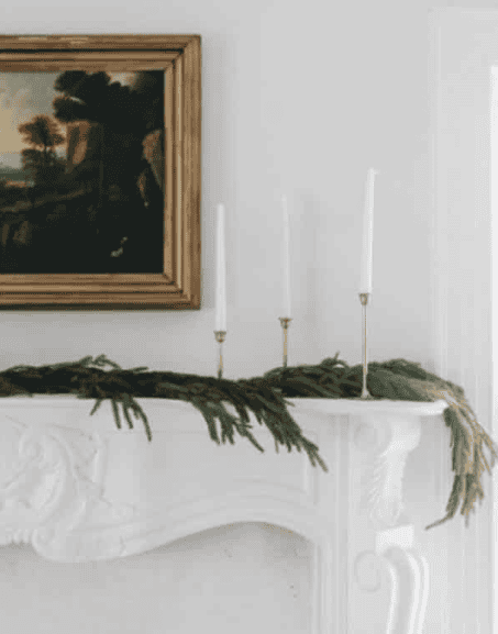 Budget-friendly festive garland draped across an Airbnb mantel, featuring pinecones and twinkle lights to create a cozy, inviting holiday atmosphere without breaking the bank.